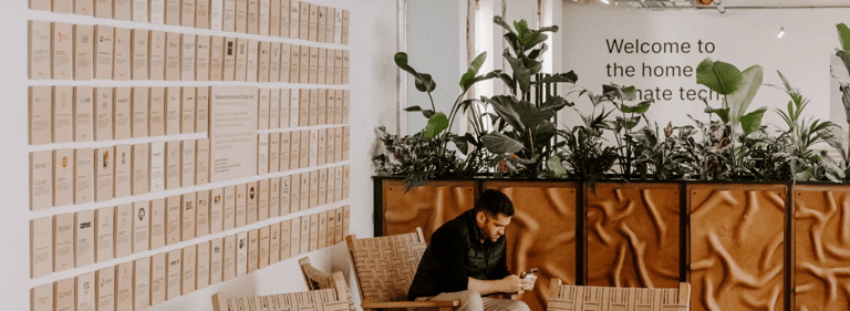 Open-plan Sustainable Ventures office space with founders working at shared desks, glass meeting rooms in the background, and sustainability-focused branding on the walls, reflecting a collaborative climate tech hub.